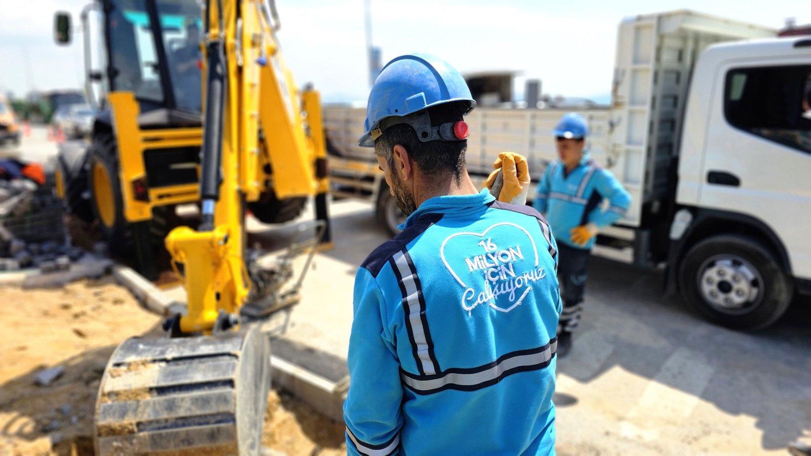 Construction workers operating excavator at a road site, ensuring progress and safety.